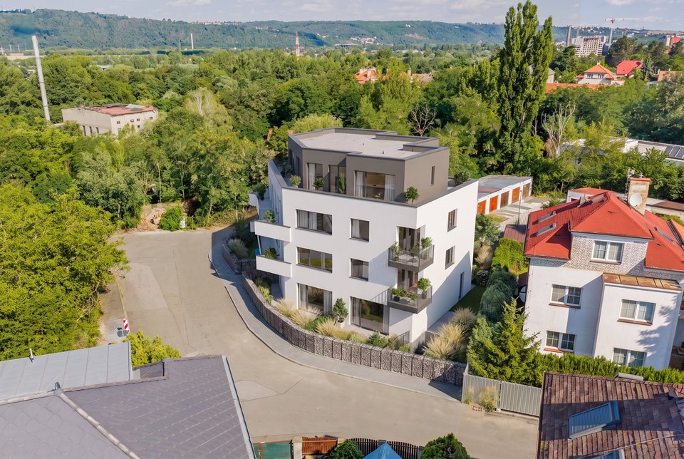 Letecký pohled na Viladům Okružní - moderní bílá budova nad zelení, řekou a okolní zástavbou